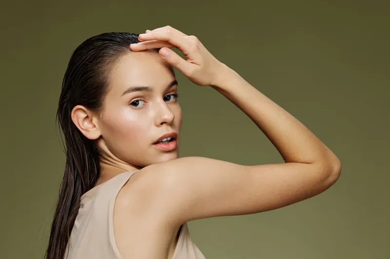 Female model with wet hair posing against a green background, showcasing natural beauty and confidence, ideal for health and wellness themes