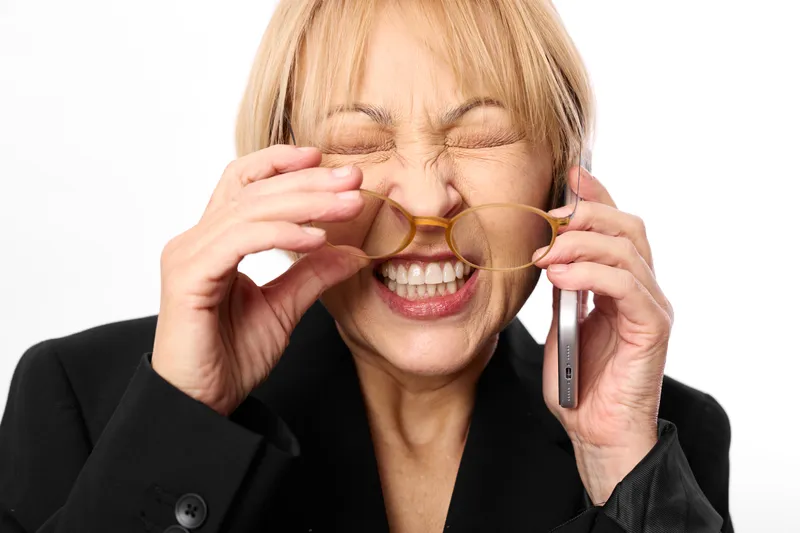 Woman phone smile laughing senior glasses studio business communication, bright light, close up portrait, relaxed posture, clean background, joyful moment in studio