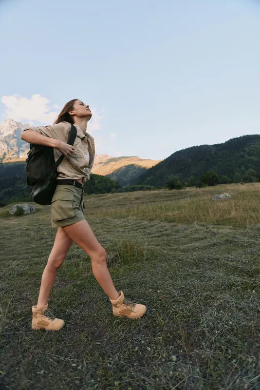 Woman hiker enjoys outdoor lifestyle, wearing shorts boots and backpack, walking on a mountain trail at sunrise, conveying freedom energy and adventure