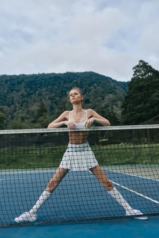 Confident young female tennis player in sporty attire showcases athleticism on outdoor court with scenic mountains in background, emphasizing health and action