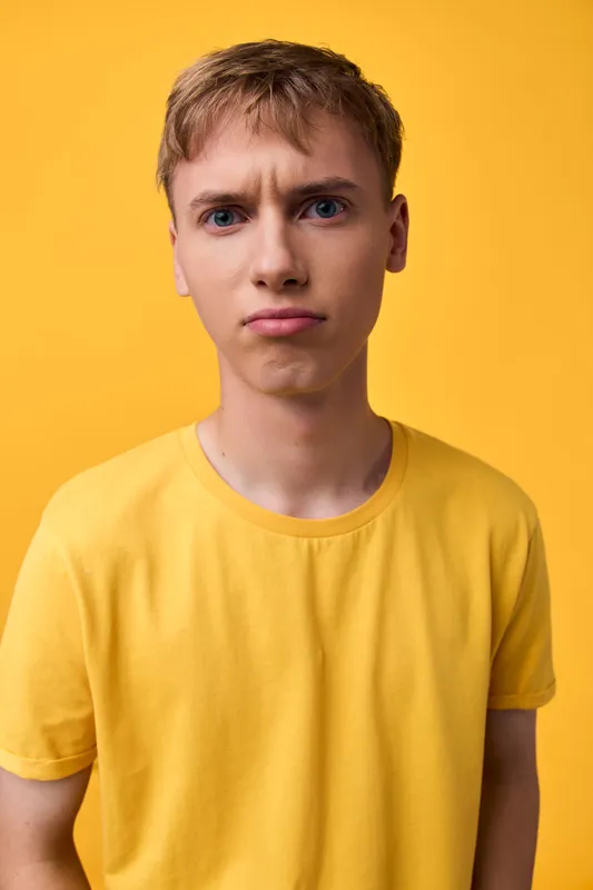 Confused expression on a young man wearing a yellow shirt against a bright yellow background, close up frame, casual style, front view, studio shot, minimal setting and mood.