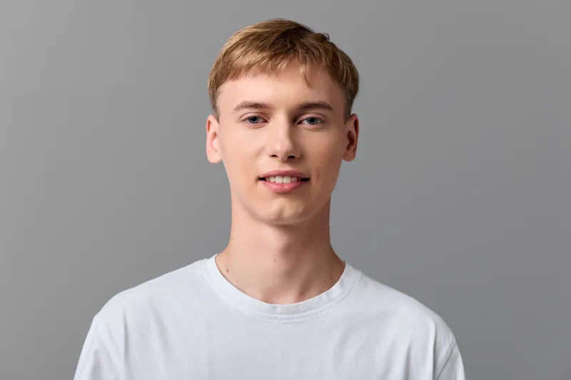 Young man with a friendly expression wearing a white t shirt stands against a neutral gray background, showcasing casual style and relaxed mood for fashion or lifestyle photography