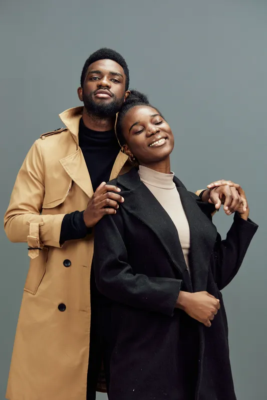Stylish couple in fashionable clothing sharing a joyful moment against a muted gray background, embodying modern love and connection through emotion
