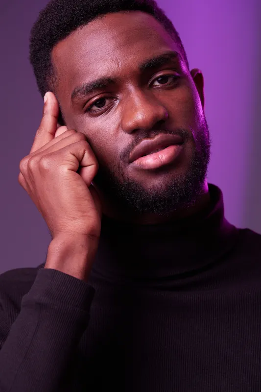 Portrait of a thoughtful young Black man in a turtleneck sweater with a serious expression against a purple background Emotional and stylish concept