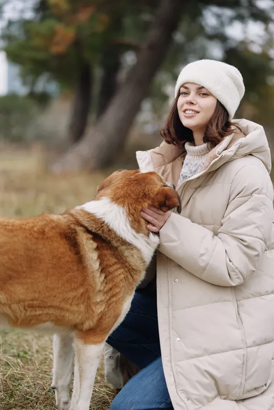 Dog, woman and warm coat outdoors in a park, affectionate moment during autumn with a friendly dog and smiling owner enjoying nature.