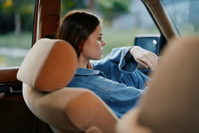 Thoughtful young woman in blue denim jacket relaxing in car interior, capturing a moment of serenity and contemplation.
