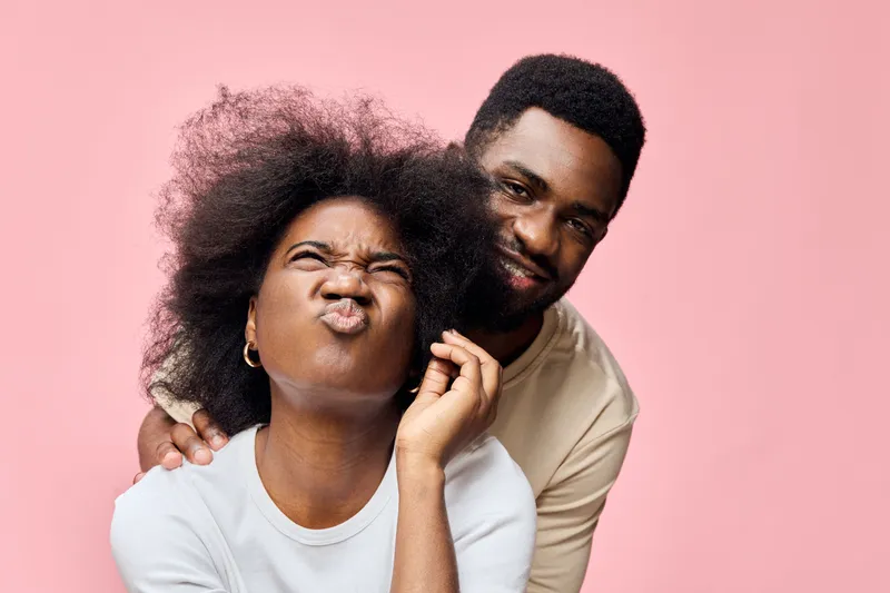 Happy couple with natural hair expressing joy against a pink background, showcasing love and fun in a stylish and playful moment