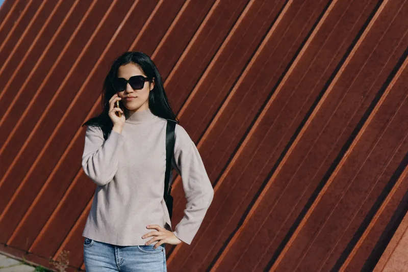 Sunglasses, sweater, street fashion on a relaxed model standing beside a corrugated wood wall, urban style and confident pose captured in soft daylight