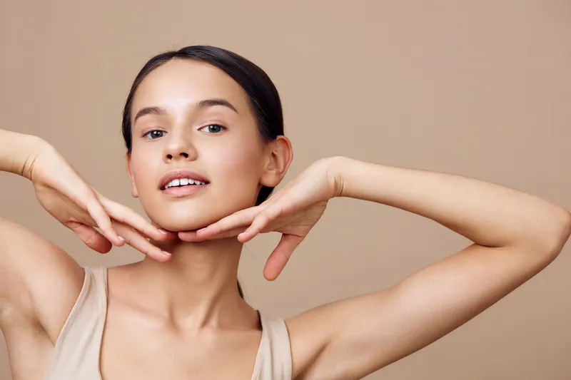 Portrait of a young woman with smooth skin, showcasing natural beauty and confidence, dressed in a light top against a neutral background