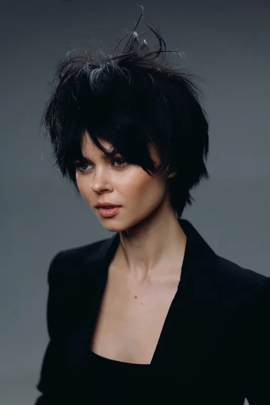 portrait of a woman with short black hair wearing a black blazer, serious expression, studio background