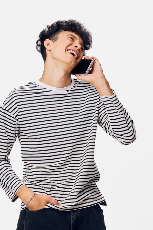 young man talking on phone, smiling with joy, wearing striped sweater, casual style, isolated white background, bright and lively mood