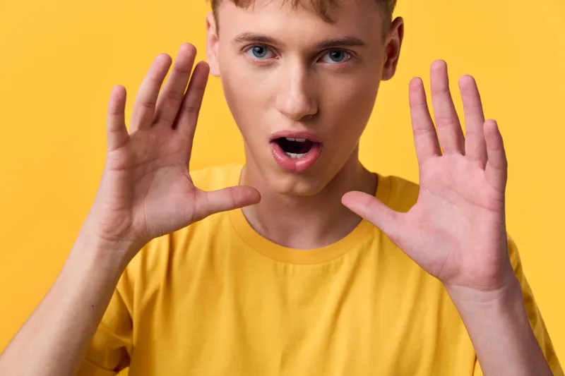 Surprised expression with hands framing face, yellow shirt against vibrant backdrop, energetic mood and closeup moment, dynamic pose, bold lighting, candid fashion shot conveying astonishment and