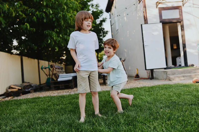 Two joyful boys playing in the backyard, having fun outdoors in a sunny environment, embracing childhood spontaneity and laughter.