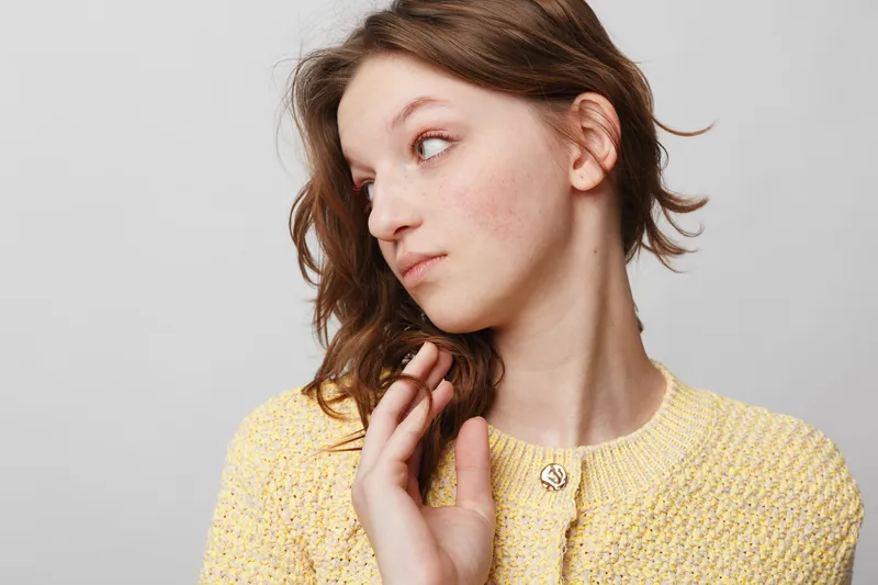 Young woman with natural skin and brown hair looks sideways wearing a yellow knitted sweater. Studio portrait on grey background with soft lighting and casual style concept.