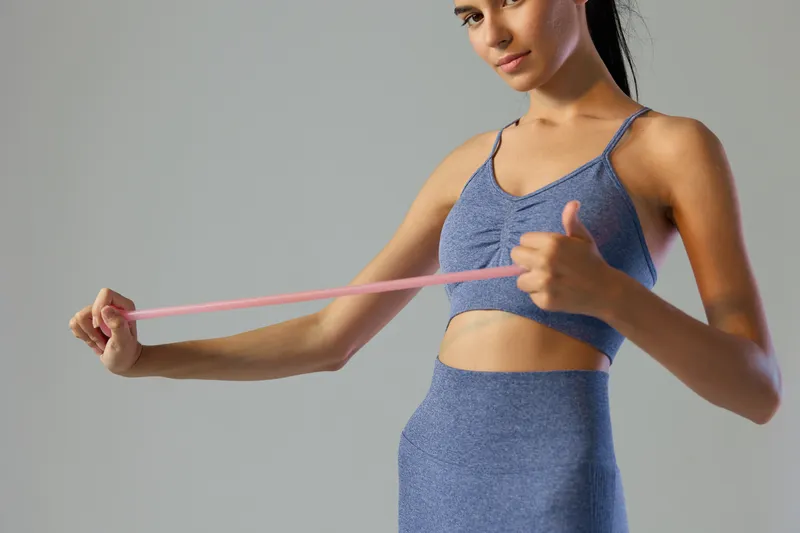 woman sport fitness stretching with resistance band in blue activewear, focused expression, toned arms, isolated neutral background