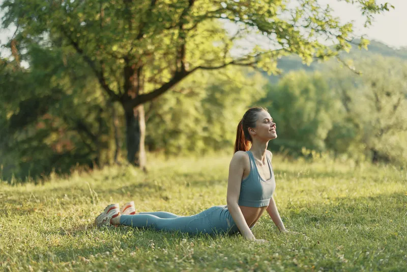Young woman in yoga pose on green grass, enjoying nature, wearing sports clothing, embracing relaxation and mindfulness in a sunny outdoor setting