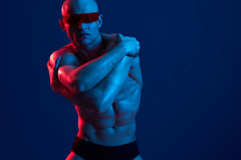 Athletic man in a dramatic pose wearing a red visor, showcasing striking blue and red lighting, creating a visually impactful black and white image.