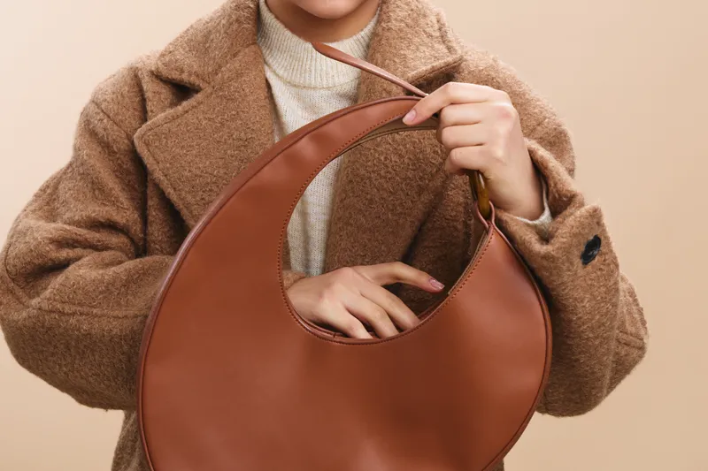 asian woman exudes confidence as she models a chic outfit and a round leather handbag in a clean studio setup, capturing a modern lifestyle moment.