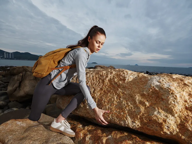 Young woman climbing on rocks in an outdoor setting, wearing casual athletic attire, representing an adventurous spirit and a healthy lifestyle