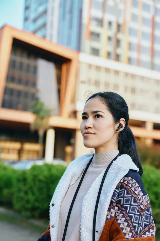 Headphones, woman outdoor cityscape fashion with jacket and scarf, daytime light, relaxed mood, urban style and travel vibe in lively street scene