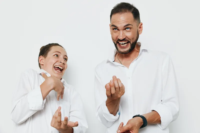 A confident business professional man and smiling colleague stand against a clean isolated white background, expressing enthusiasm, energy, and collaboration through dynamic gestures.