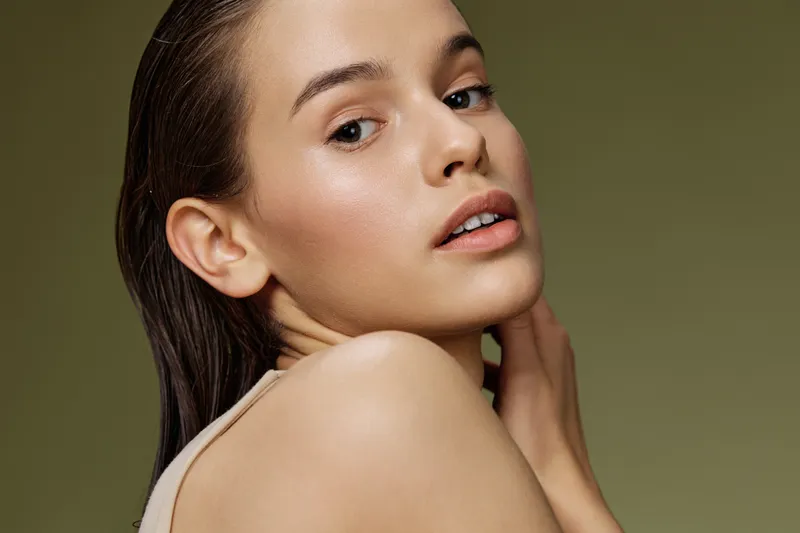 Portrait of a young woman with natural makeup, soft skin texture, and a subtle expression against a green background, emphasizing beauty and self care concepts