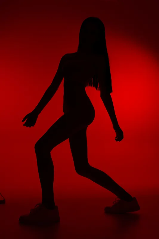 Silhouette of a woman sport fitness exercising in dynamic pose against vibrant red background, emphasizing strength, motion, and athleticism in a modern studio setting.