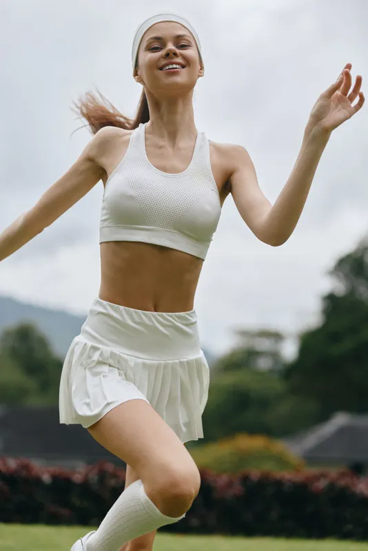 Young athletic woman in white sportswear joyfully running outdoors in a natural green environment, embodying energy and fitness