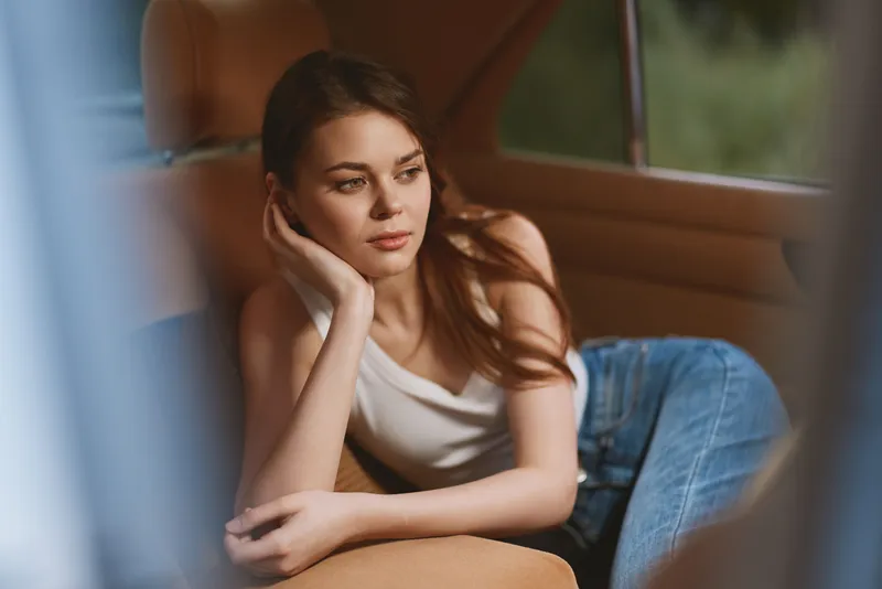 Thoughtful young woman in casual attire relaxing in a car, evoking a sense of tranquility and contemplation with a blurred green background.