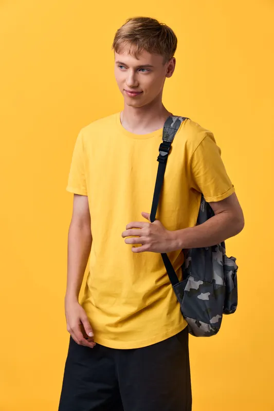 Young male with a yellow tshirt and backpack stands against a vivid yellow backdrop, showcasing casual youth fashion and streetwear style, ready for travel and daily activities
