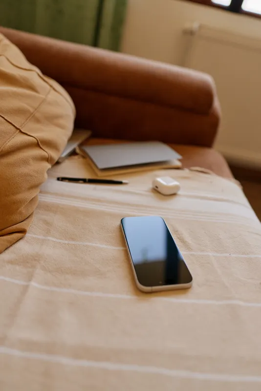 Smartphone rests on a striped bedspread beside a sofa, capturing a casual home lifestyle moment centered on daily technology use and relaxed comfort.