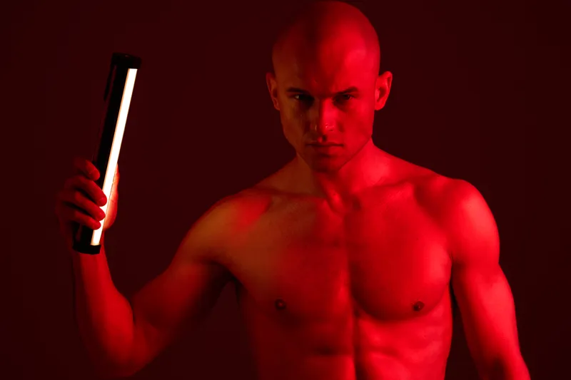 Strong man holding a flashlight in a dramatic light, showcasing intense emotions and powerful physique, set against a rich dark background.