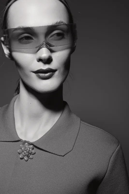 Close-up portrait of a pale caucasian woman wearing futuristic glasses and a collared top with a brooch. Concept of fashion, style, and modern elegance in monochrome.