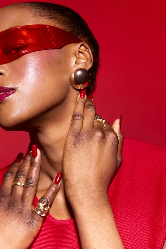 Close-up of elegant dark skinned African woman wearing red top and red translucent visor, with glossy skin and red manicure. Concept of fashion, beauty, style, and modern accessories.