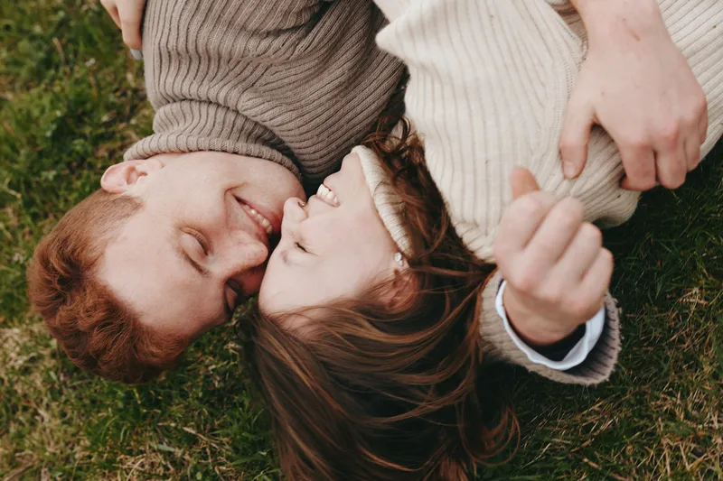 couple outdoors laughter smile grass sweater nature portrait lifestyle intimate field sunlight moment relaxed candid connection warmth ease joy pair light breeze clothing texture blanket grassland