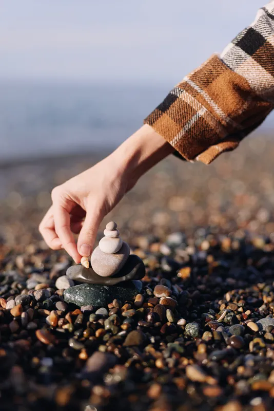 Mindful moment at the beach as a hand stacks smooth stones on a pebble shore beside the sea, conveying balance, patience and focus in nature and serenity of coast.