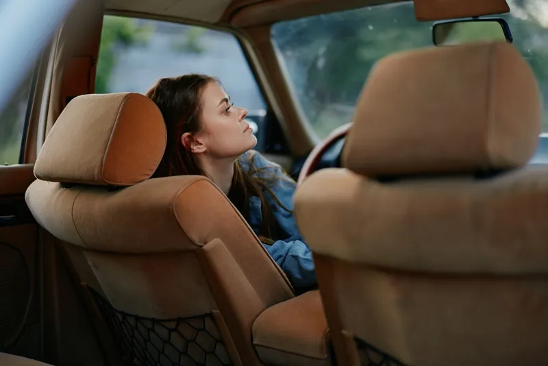 Thoughtful woman sitting in a vintage car interior, reflecting and enjoying the soft natural light, with warm earthy tones creating a nostalgic mood.