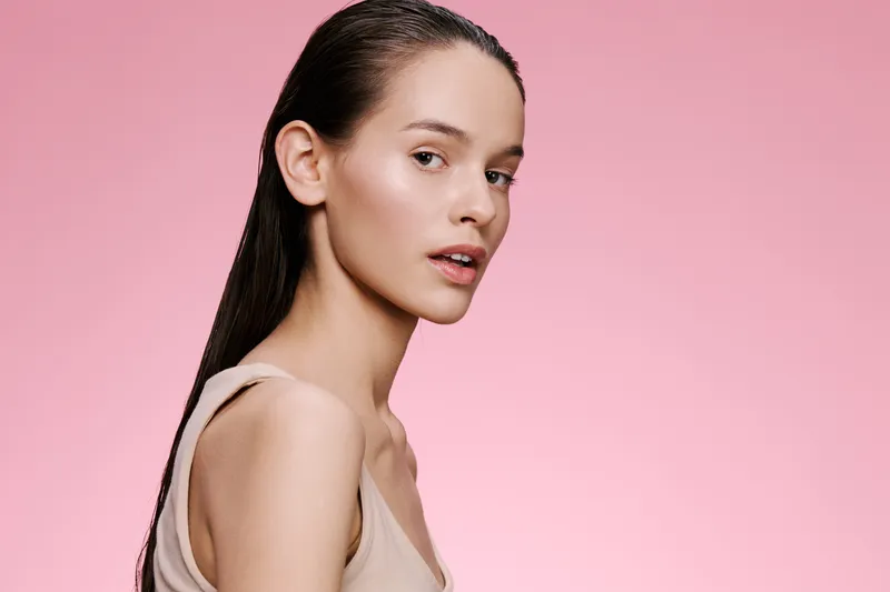 Elegant young woman with wet hair against a soft pink background, showcasing beauty and fashion Perfect for health and skincare themes