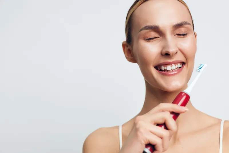 Smiling woman holding a toothbrush in a bright studio setting, emphasizing oral hygiene and dental care. Close, upbeat moment highlighting health, self care, and a clean, radiant smile.