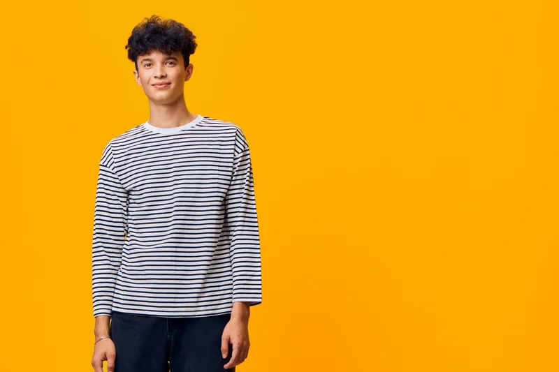 young man smiling wearing striped shirt standing against vibrant orange background, casual style, friendly expression, modern portrait