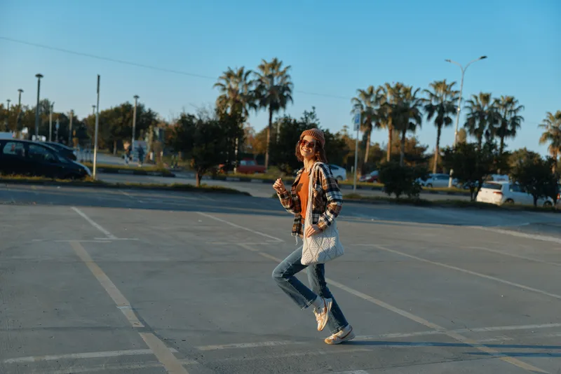 Woman running in parking lot at sunset with palm trees, candid lifestyle portrait capturing authenticity and golden hour glow, joyful motion and emotional storytelling in urban mindful living.