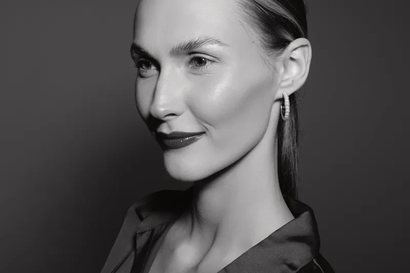 Close-up of a smiling young white woman with light skin and slicked back hair wearing hoop earrings against a dark background. Concept for beauty, elegance, and portrait photography.