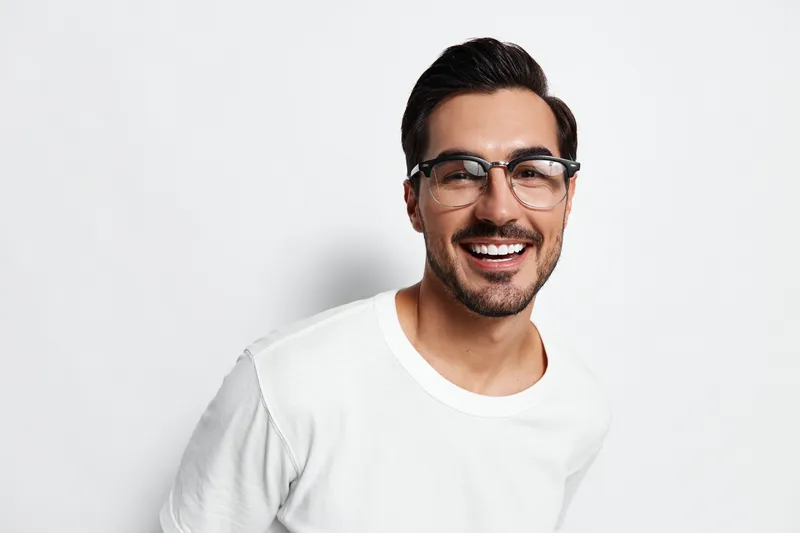 Smiling man in casual white t-shirt and glasses, looking at the camera with a cheerful expression, against a plain solid white background. People lifestyle concept.