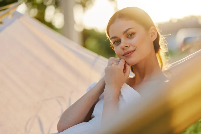 Young woman relaxing in a hammock during sunset, showcasing serenity and natural beauty in a vibrant outdoor setting