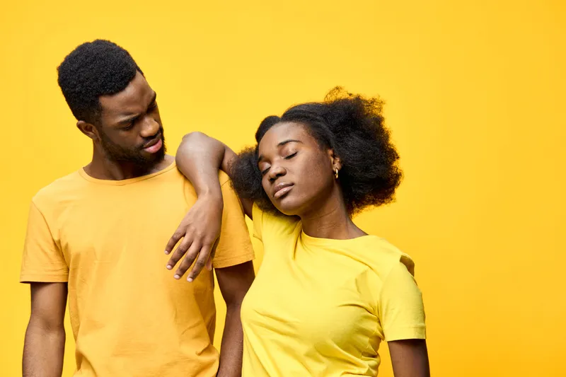 A joyful couple in yellow outfits sharing a tender moment against a bright yellow background, expressing warmth and love Their emotions radiate happiness and connection