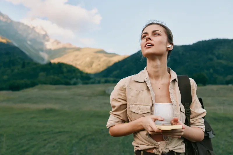 Young woman traveler with backpack holding map looks up enjoying nature outdoors in mountains during sunny day, lifestyle adventure concept in green landscape.