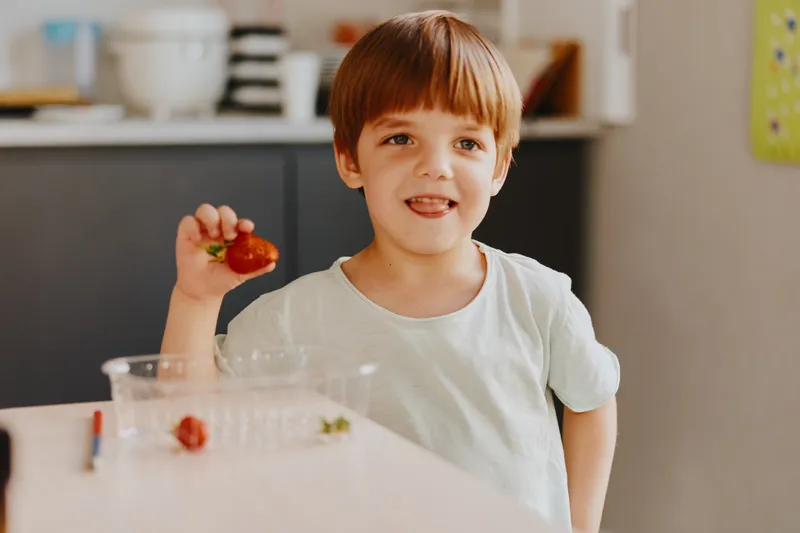 Happy boy enjoying strawberries in a bright kitchen, showing delight with a playful expression. Perfect for family and food themes.