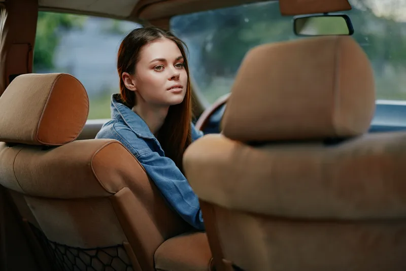 Young woman in denim jacket sitting in a car, looking thoughtfully through the windows, capturing a sense of nostalgia and freedom.