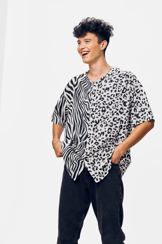 young man laughing in stylish black and white animal print shirt with hands in pockets against white background, casual confident expression, modern fashion