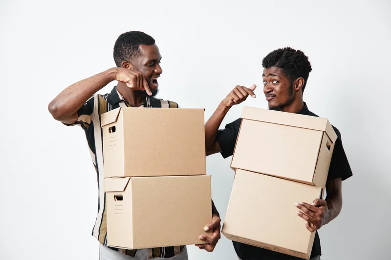 Two african men with dark skin holding cardboard boxes and smiling while standing against white background for delivery and moving concept.